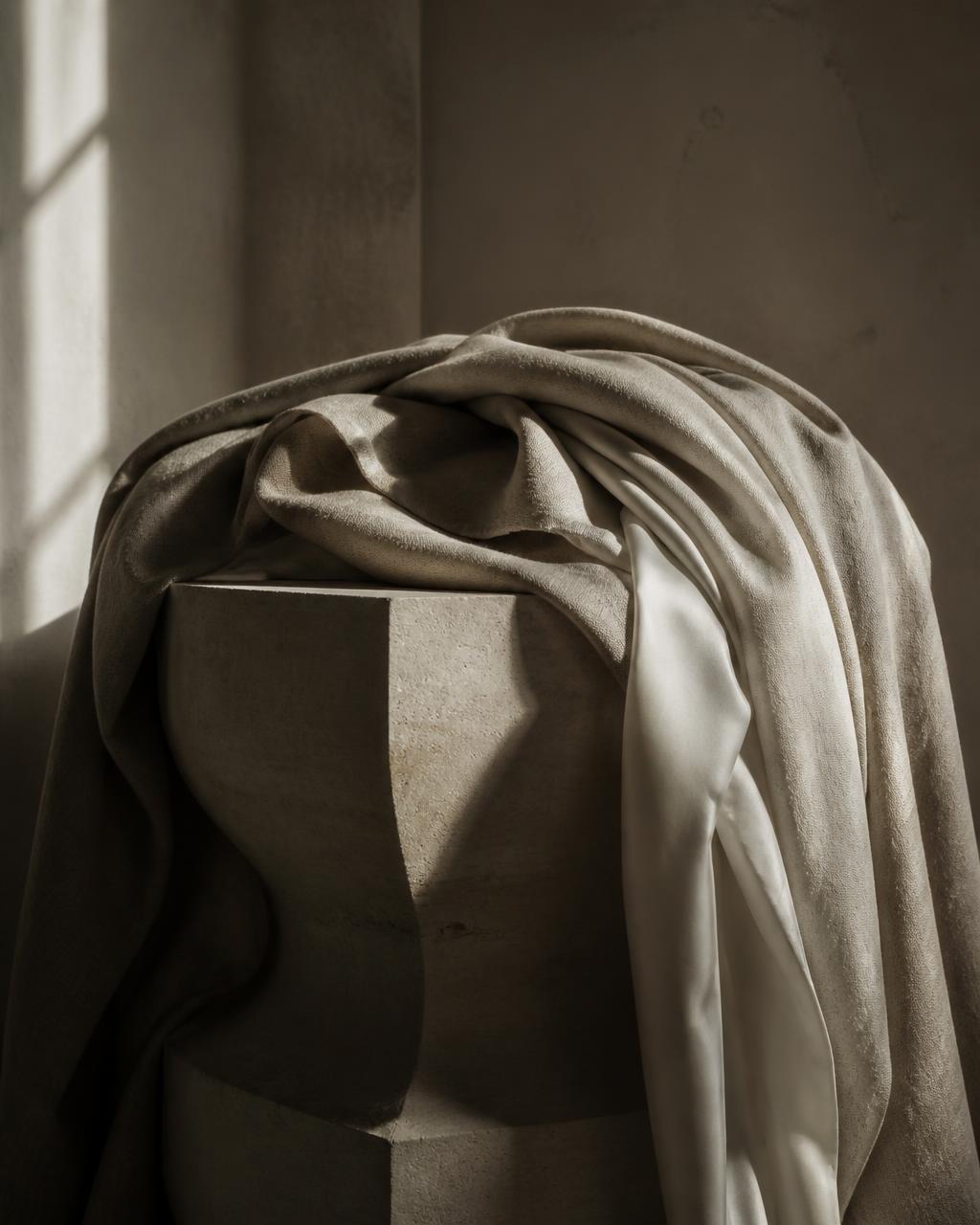 Draped linen and silk over a stone plinth in soft daylight